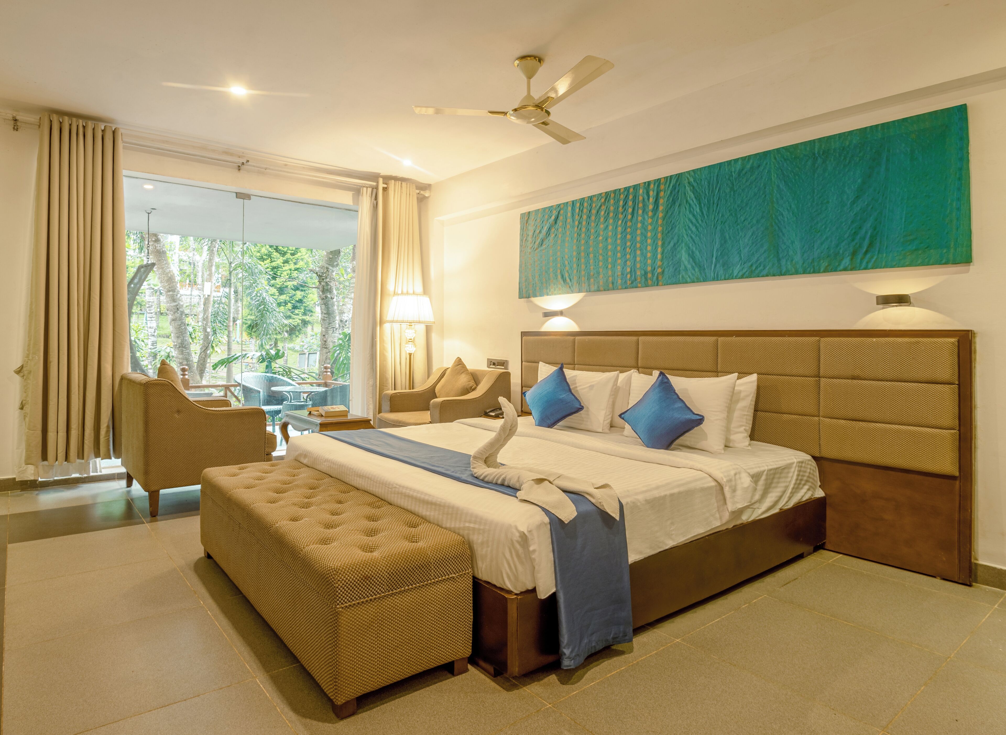 A hotel room with a large bed, a sofa, a dining table, and a view of the outdoors.