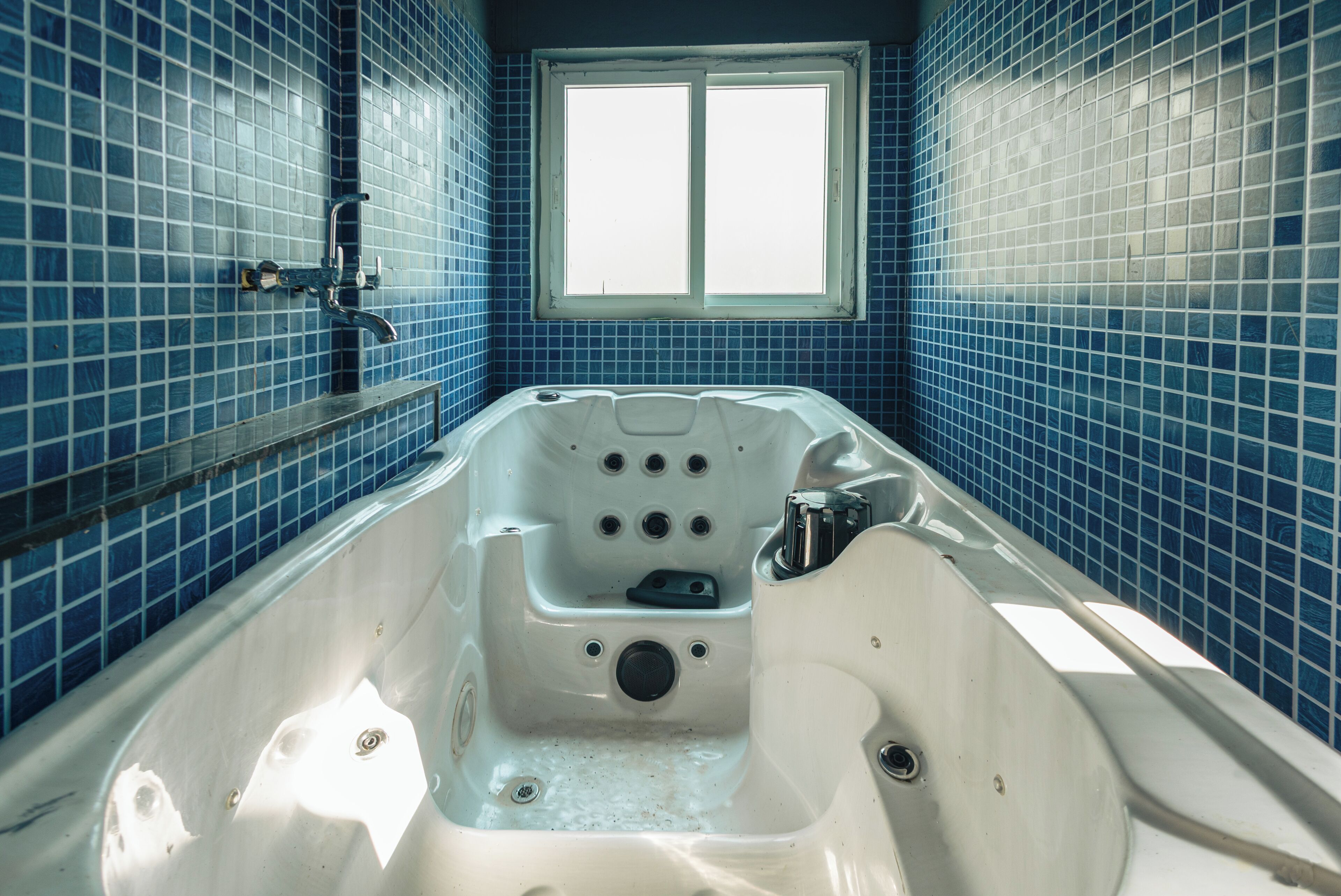 Un baño con una bañera grande, paredes de azulejos azules y un ventanal.