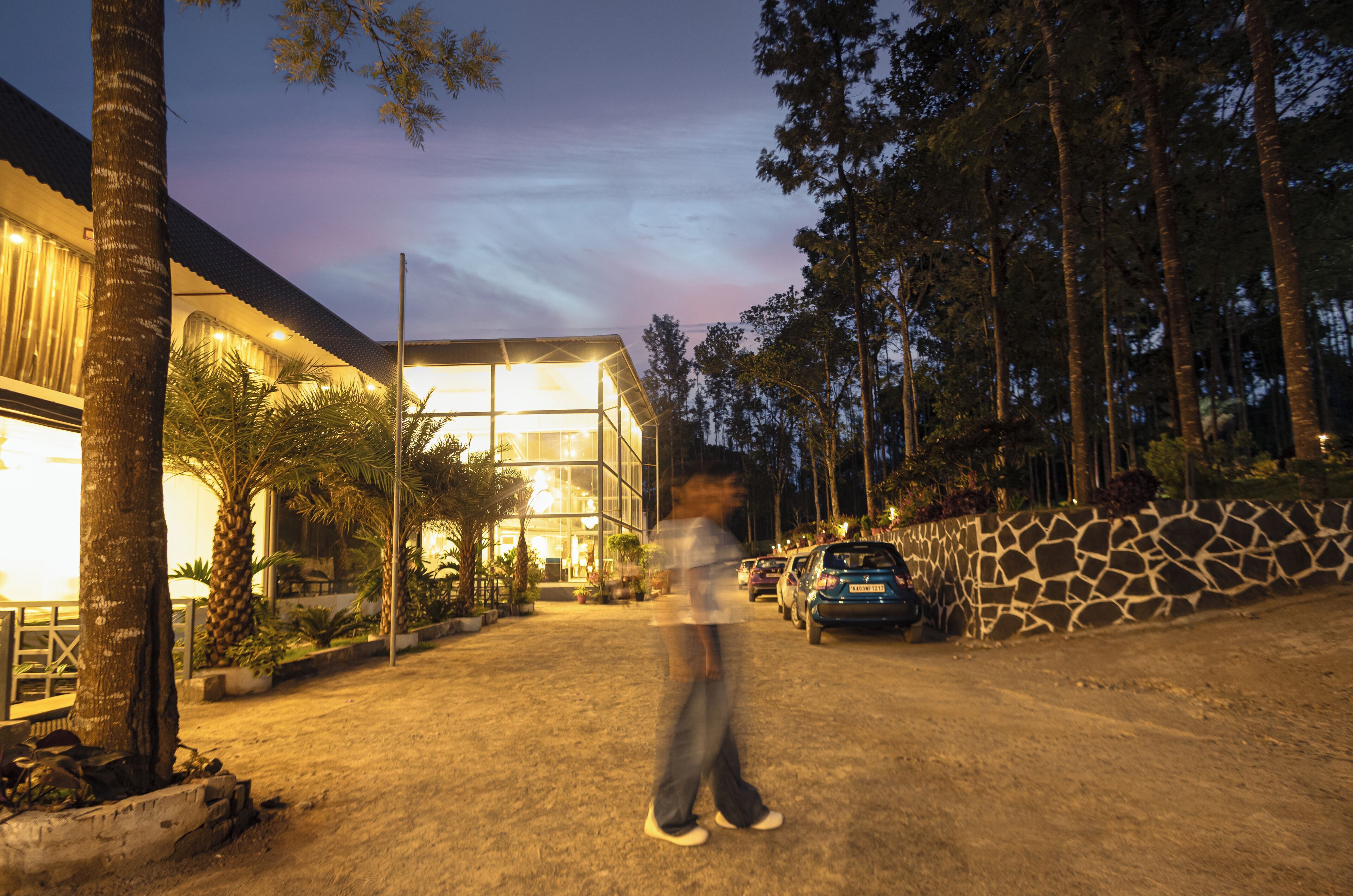A modern building with a glass facade, surrounded by trees and a stone wall.