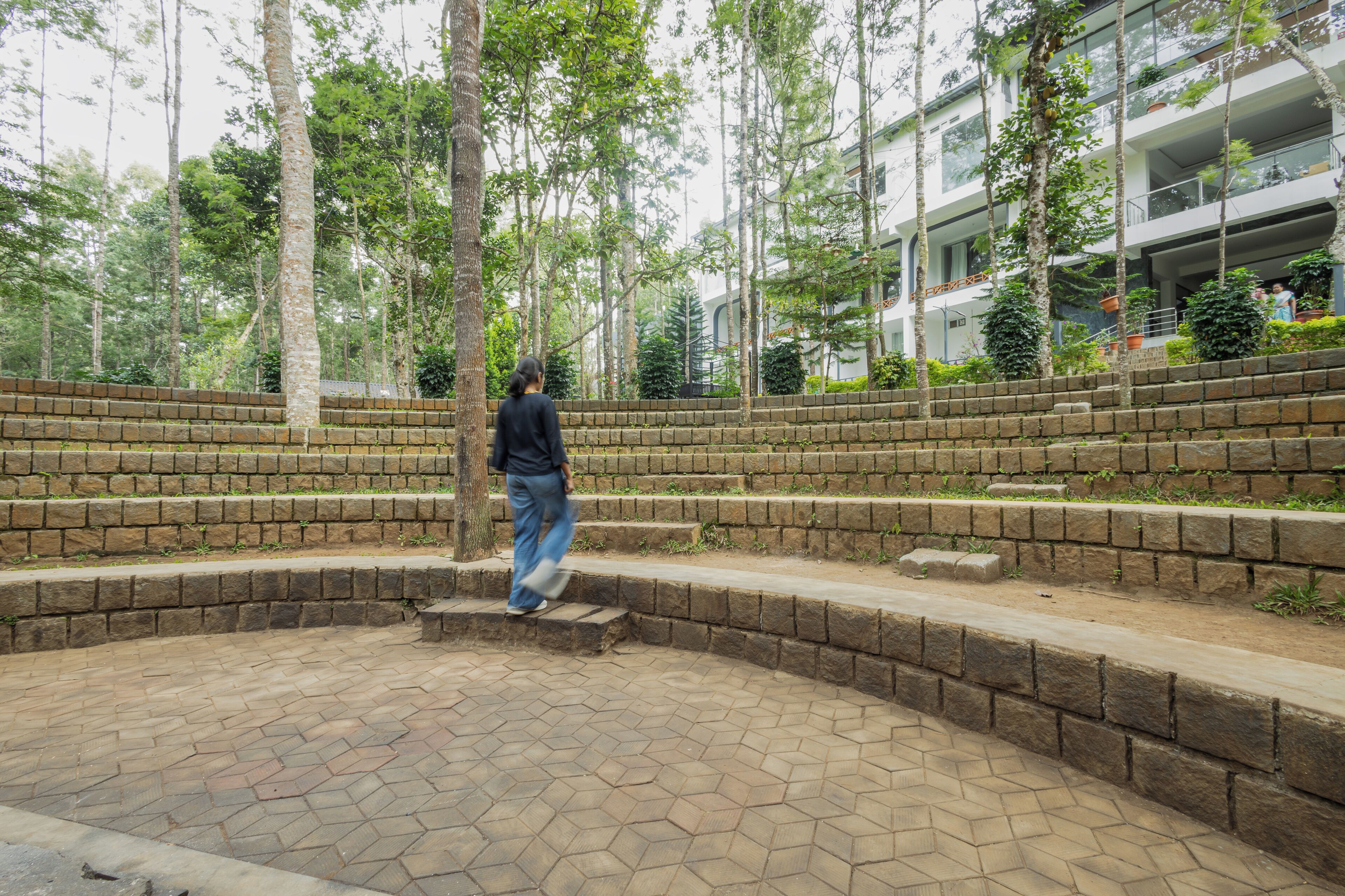 A circular stone pathway with steps leading to a central point, surrounded by trees and a building with balconies.