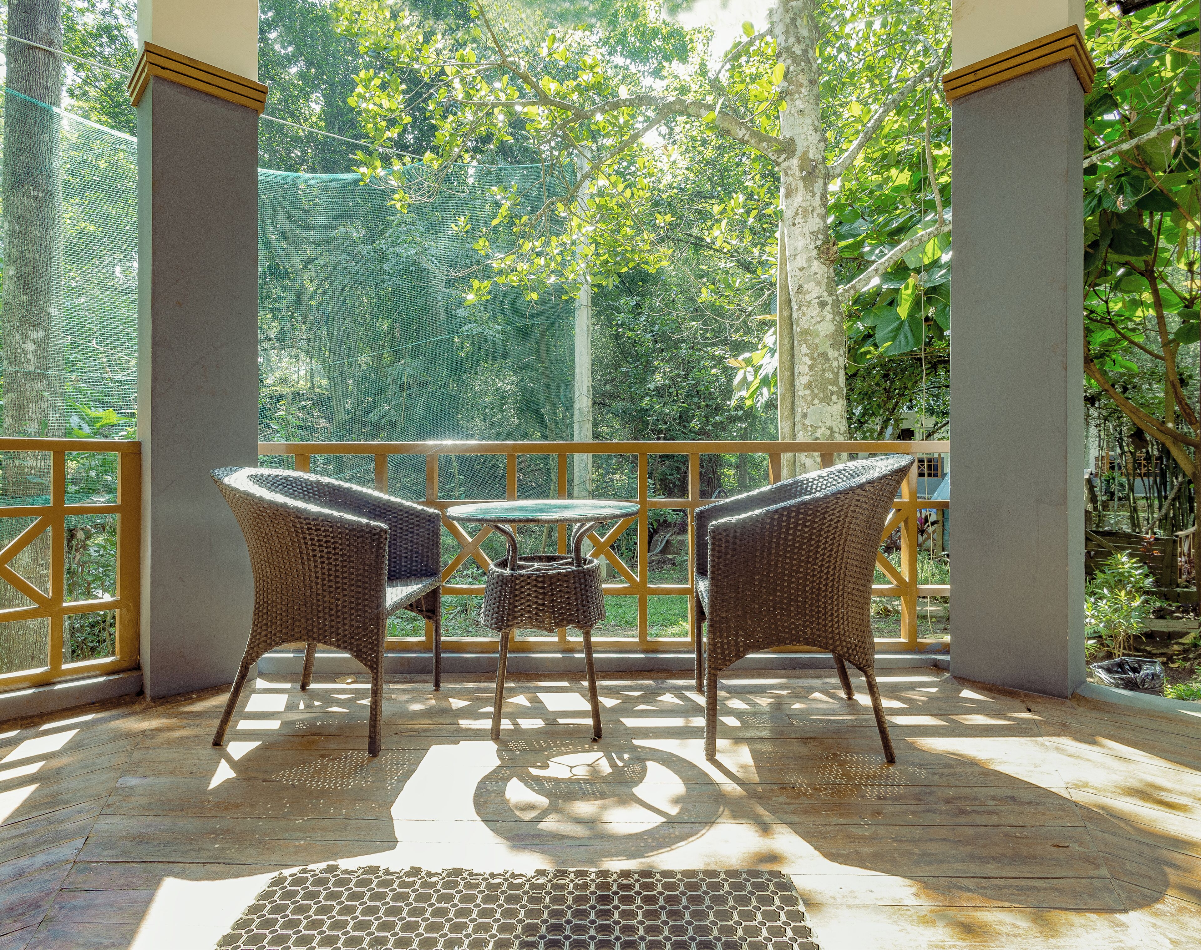 A covered outdoor seating area with wicker furniture and a table, surrounded by a wooden deck and a mesh fence.