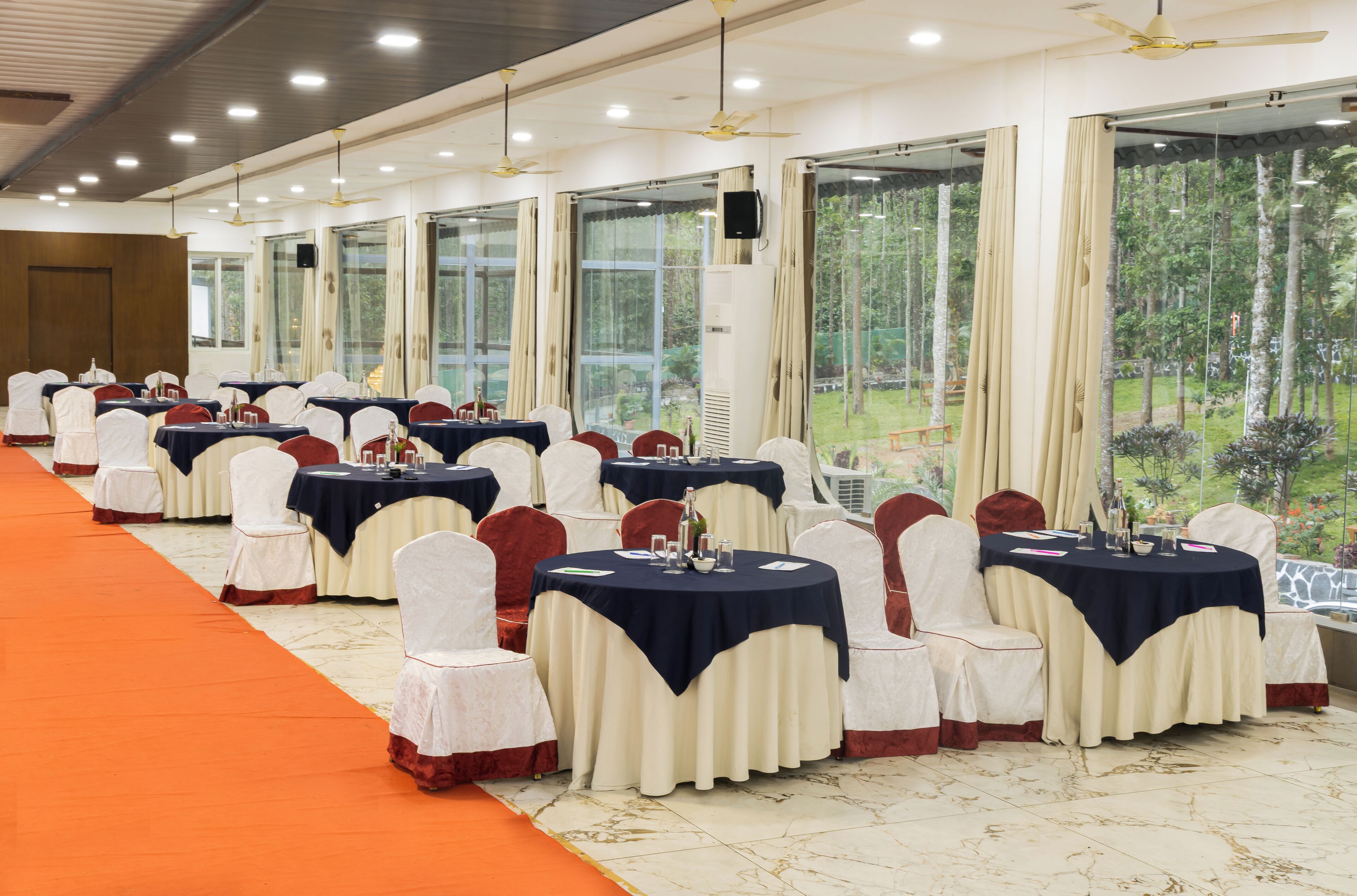 A banquet hall with round tables, white chairs, and an orange carpet.