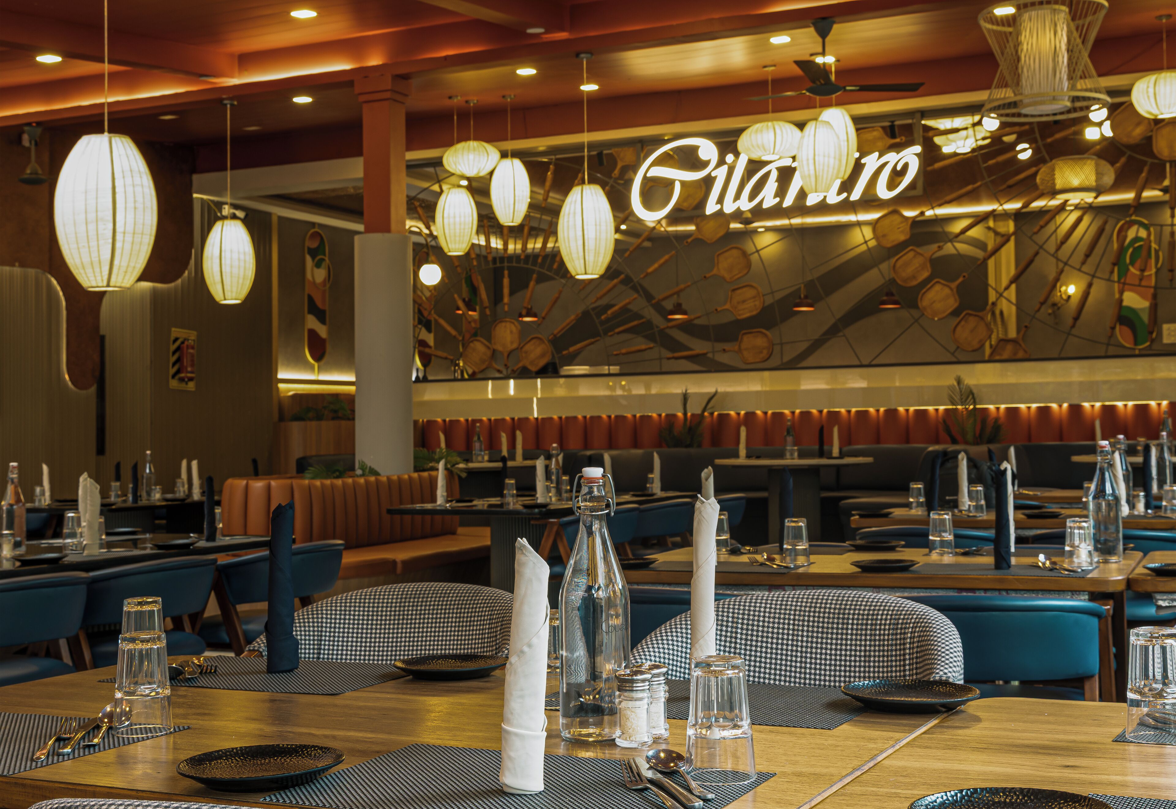 A restaurant interior with tables set for dining, hanging paper lanterns, and a neon sign.