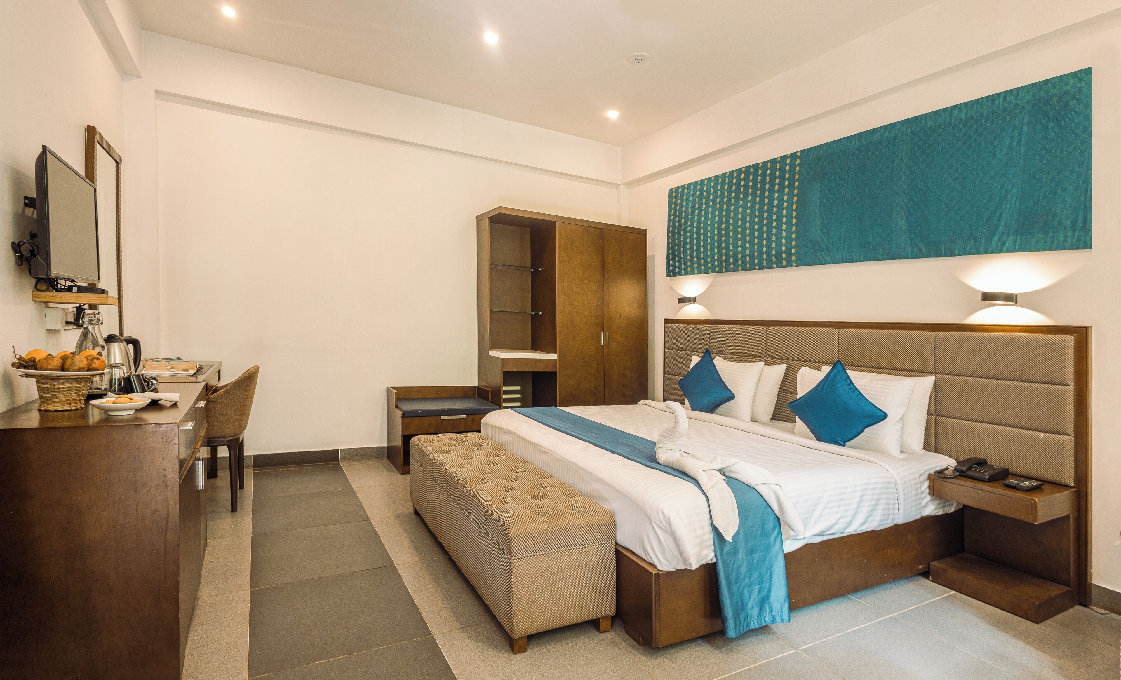 Une chambre d’hôtel comprenant un lit, des tables de chevet, un bureau avec une chaise, une armoire et une grande fenêtre.