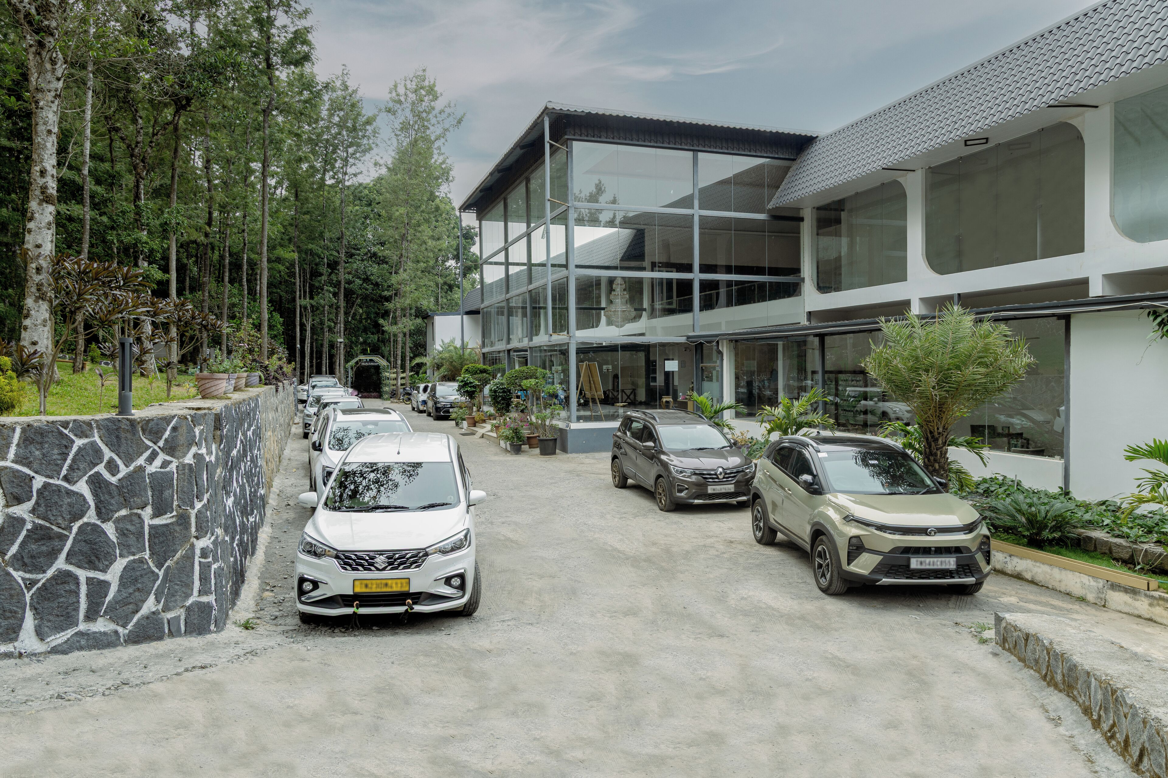 A modern building with large windows, a parking area with several cars, and a stone wall on one side.