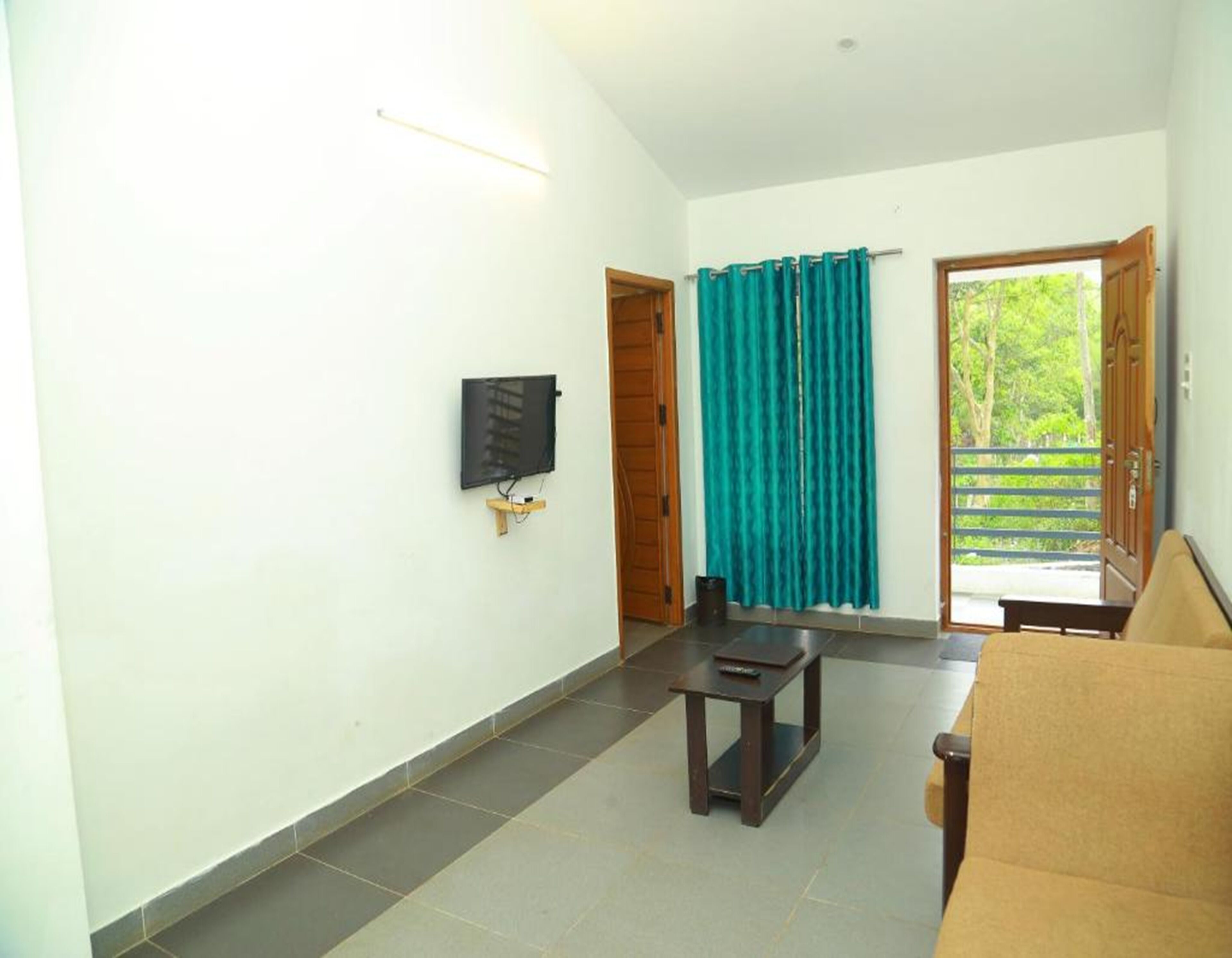 A room with a television mounted on the wall, a wooden door, a teal curtain, a small table, and a sofa.