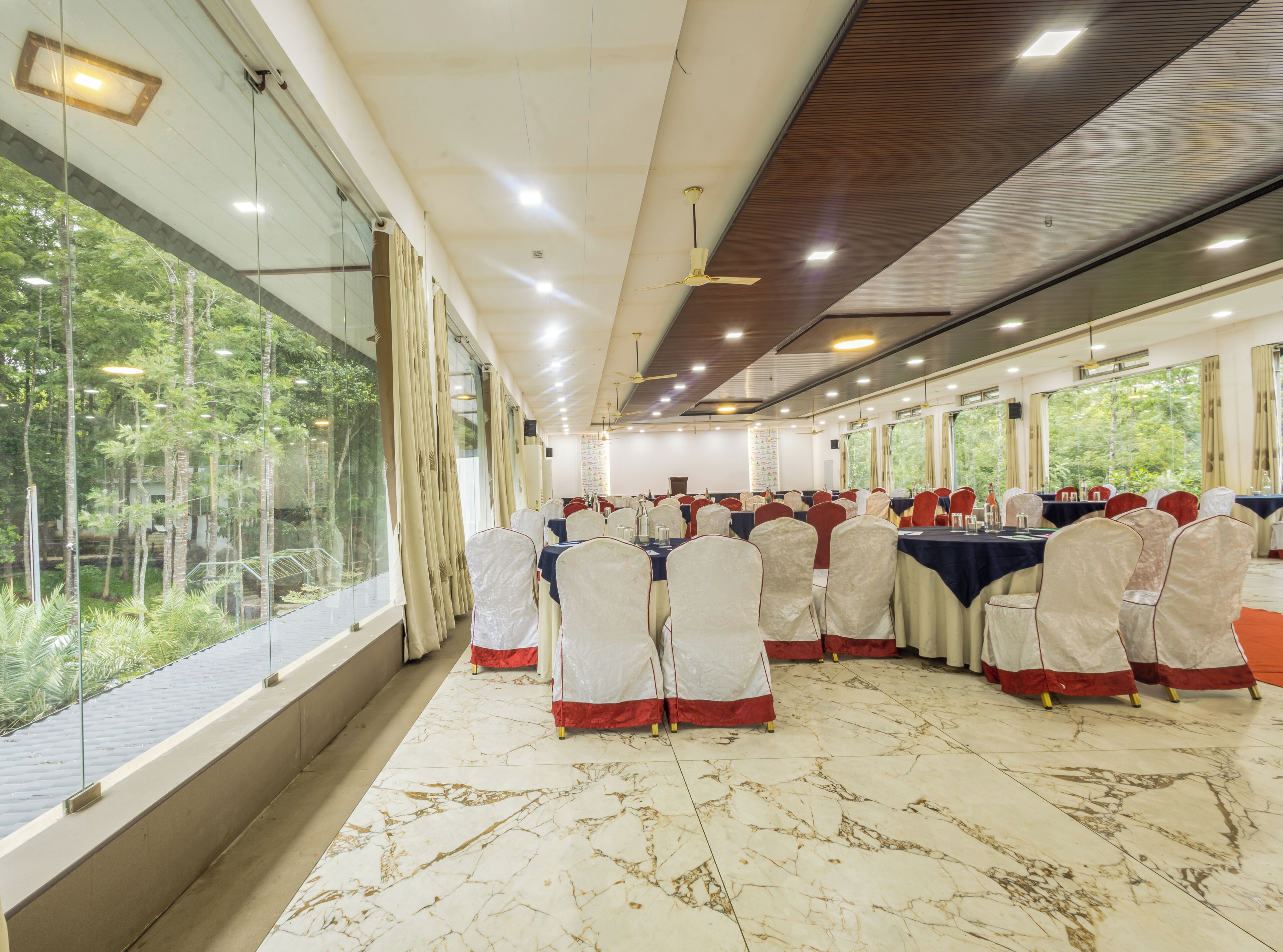 Un salón de banquetes con mesas dispuestas para eventos, amplias ventanas y un ventilador de techo.