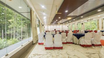 Un salón de banquetes con mesas dispuestas para eventos, amplias ventanas y un ventilador de techo.