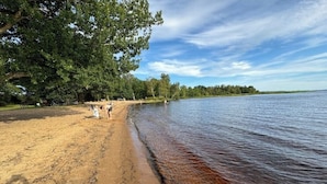 Ein sandiger Strand mit einem ruhigen See, umgeben von Bäumen.