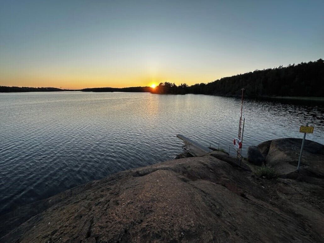A calm lake at sunset with a fishing rod and a sign on the shore.