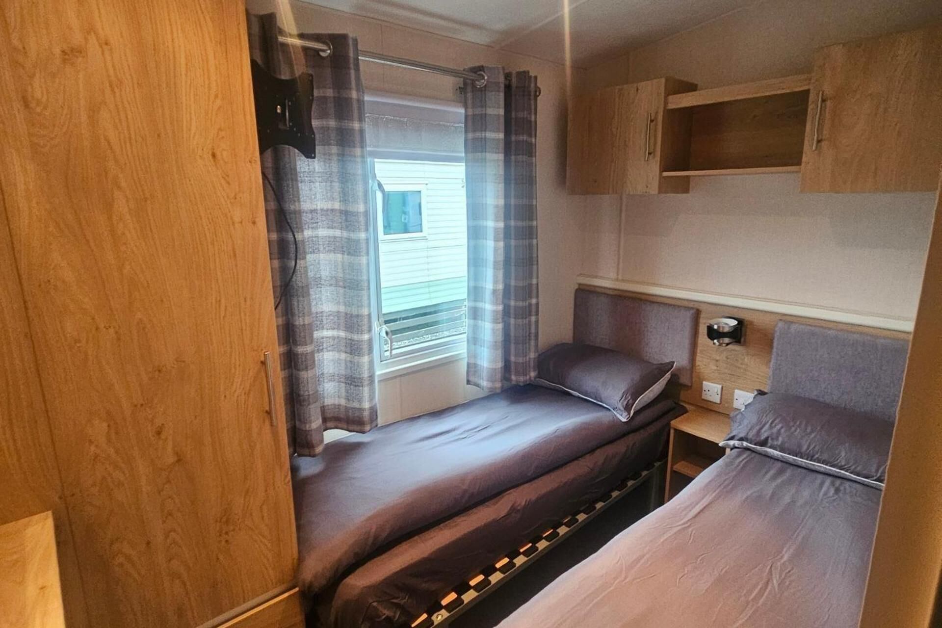 Une chambre compacte dans un camping-car, avec deux lits, une fenêtre avec des rideaux et des meubles en bois.