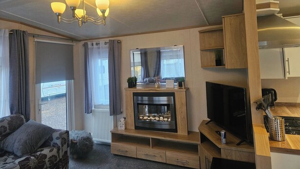A cozy living room with a fireplace, a television, and a dining area with a kitchen counter. - Dunooncaravan/2bed/sleeps4/scenicwwalks/tv/wifi (Dunoon)