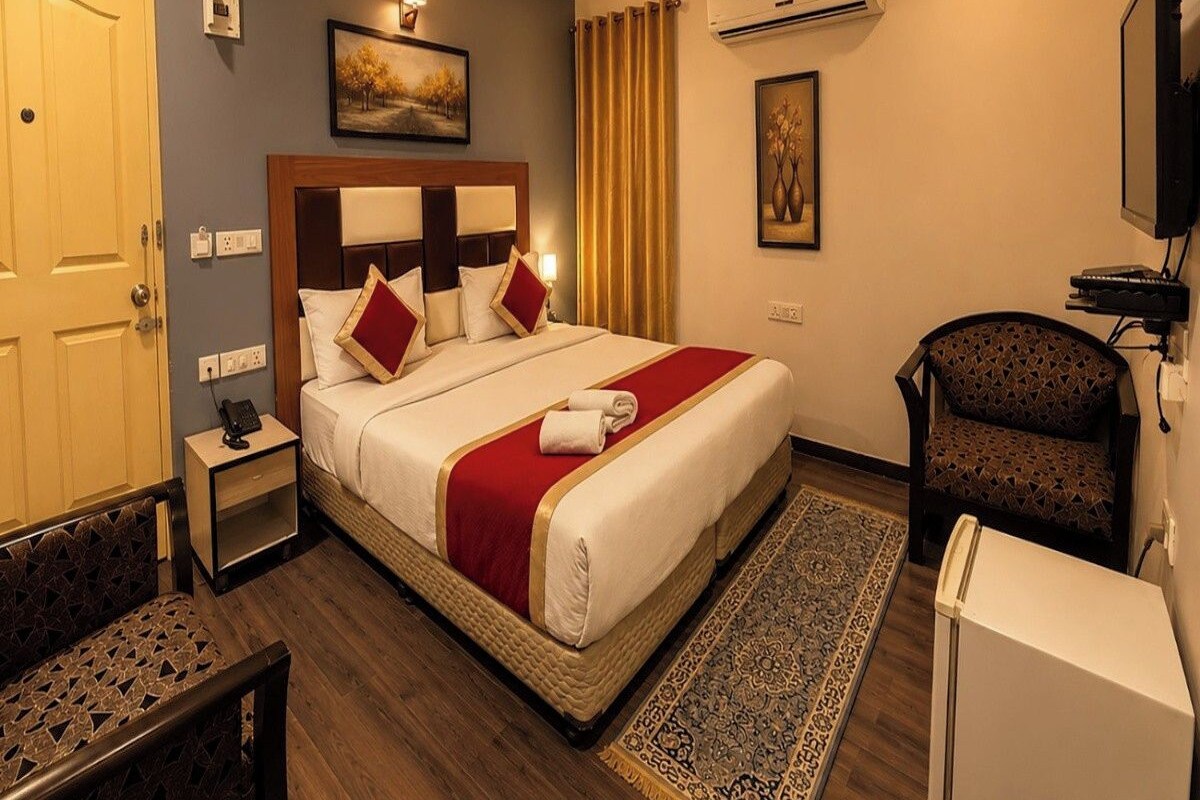Una habitación de hotel con cama, escritorio, silla, televisor y aire acondicionado.