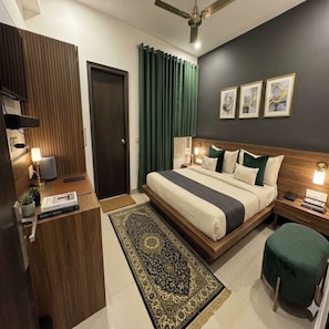 A modern hotel room with a large bed, a desk, a chair, a standing lamp, a floor lamp, a green curtain, and a ceiling fan. - Hotel The Grand Shoba  (New Delhi)