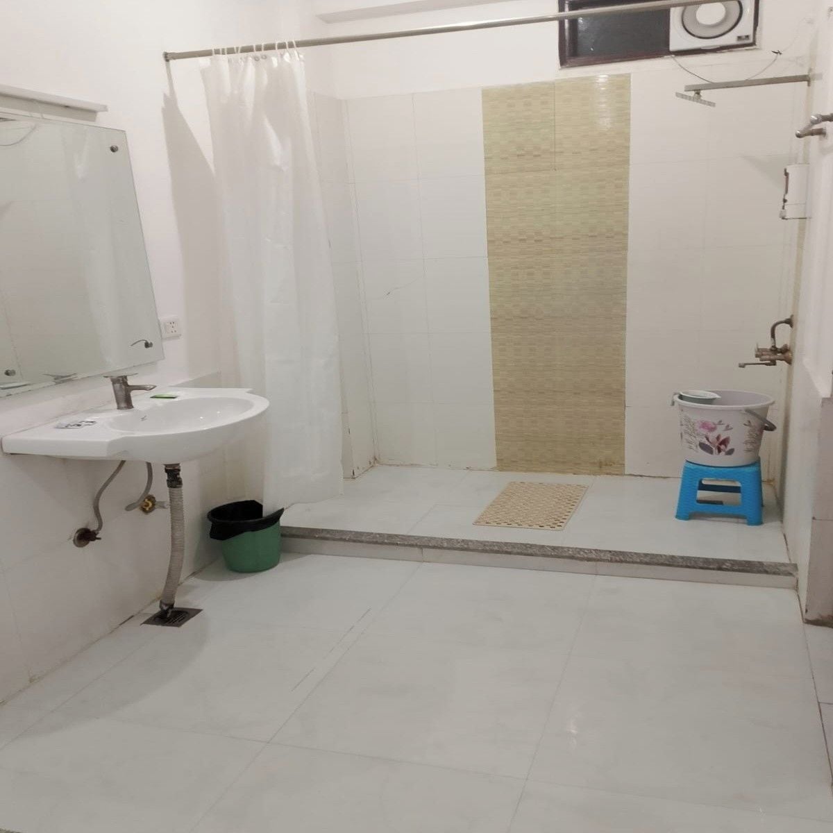 A bathroom with a white sink, a shower area, and a small blue stool.