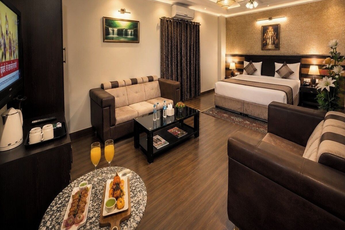 Una habitación de hotel moderna con sofá, cama, una mesa de centro con aperitivos, televisor y ventilador de techo.