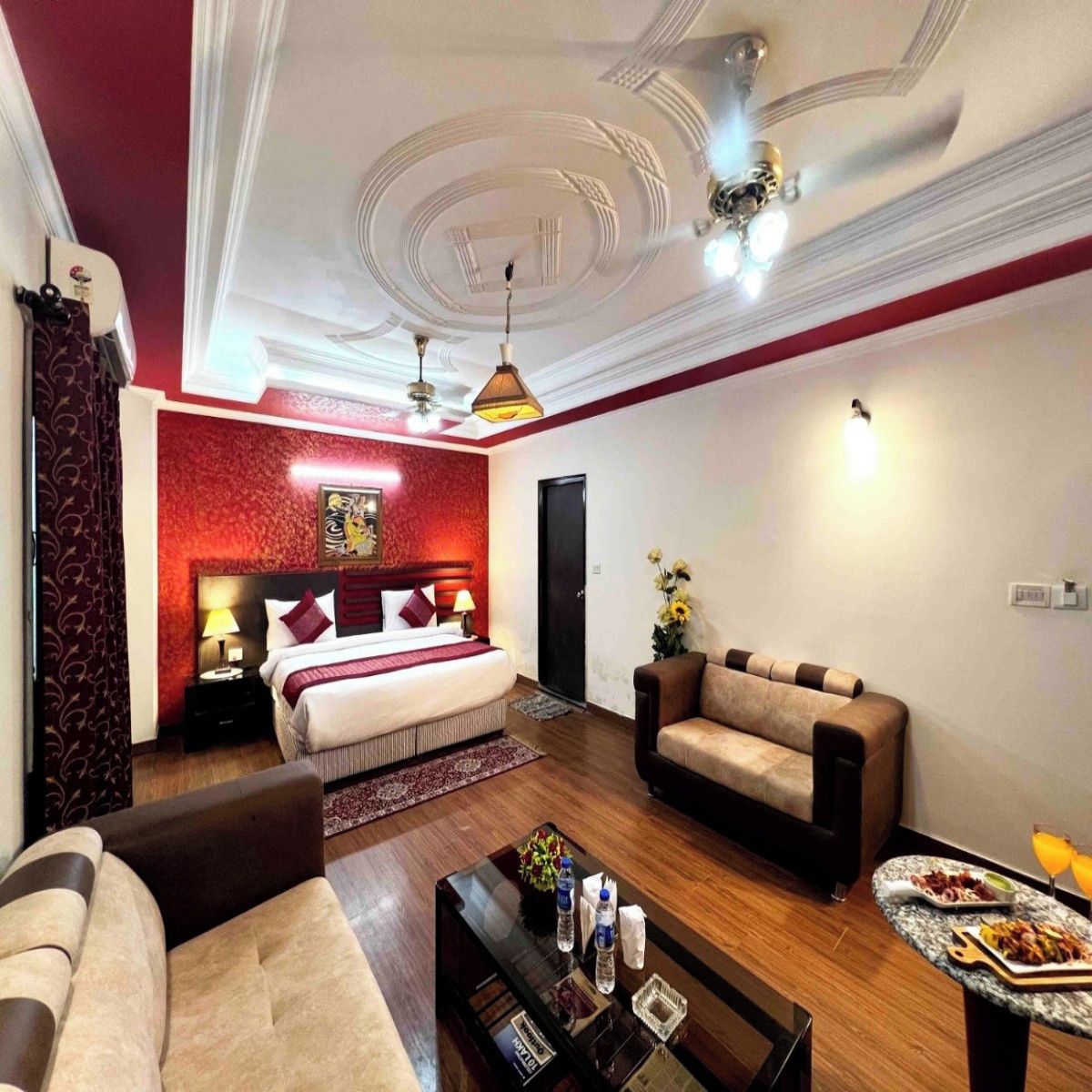 A hotel room with a bed, a sofa, a coffee table, and a dining table with food.