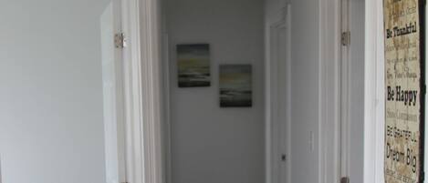 A hallway with wooden flooring, white walls, and two doors. There are two framed pictures on the wall and a sign with motivational phrases.