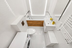 A modern bathroom with a bathtub, toilet, and a washing machine. - Lumina stylish apart with balcony (Warsaw)