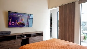 A bedroom with a bed, a TV mounted on the wall, a wooden dresser, and a sliding door leading to a balcony. - Apartamento Morelos SLP Centro Historico (San Luis Potosi)