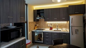 A modern kitchen with dark wooden cabinets, a gas stove, a built-in oven, a refrigerator, and a dining area with a table and chairs. - Apartamento Morelos SLP Centro Historico (San Luis Potosi)