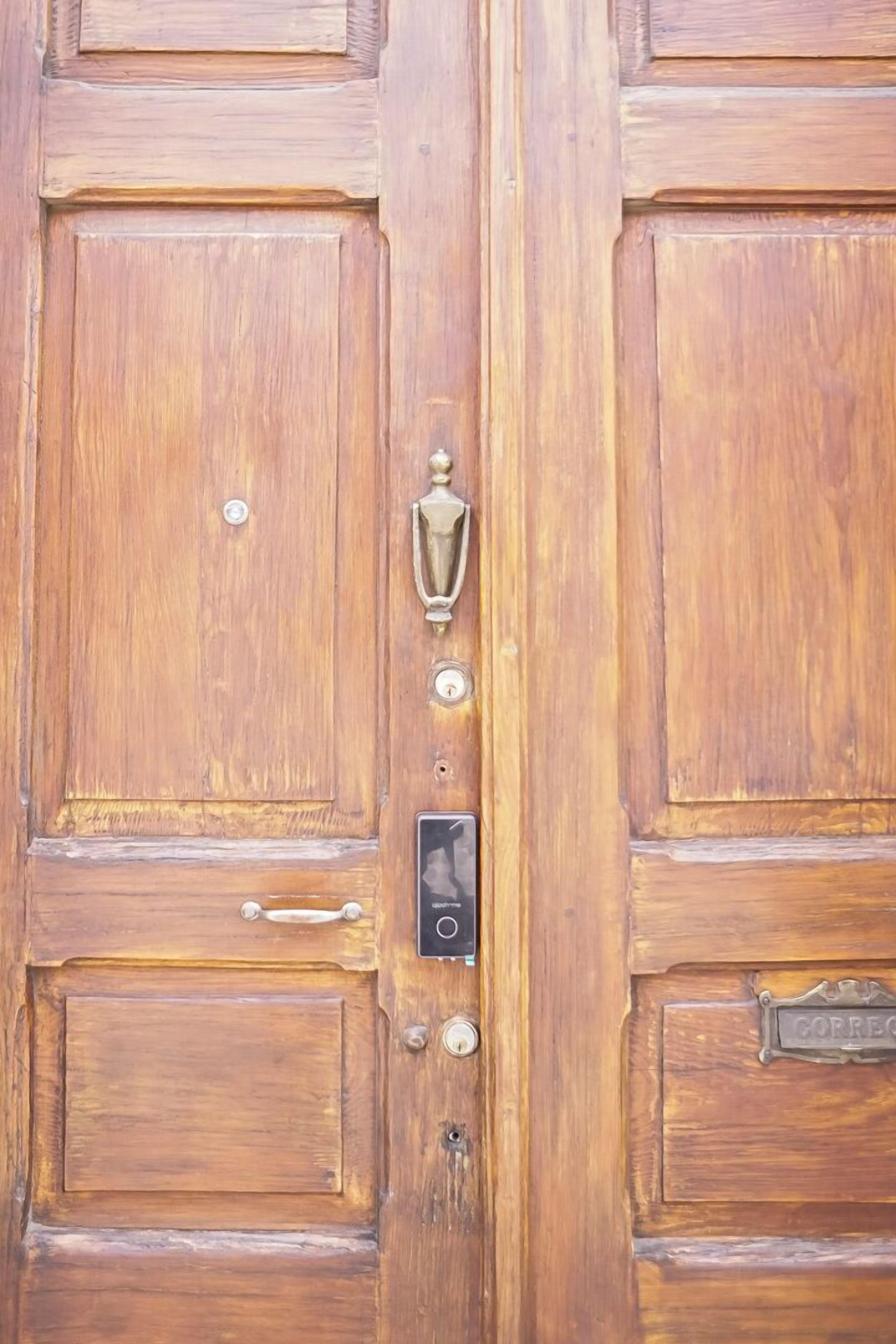 Una puerta de madera con un llamador de latón, un ojo de cerradura y un timbre.