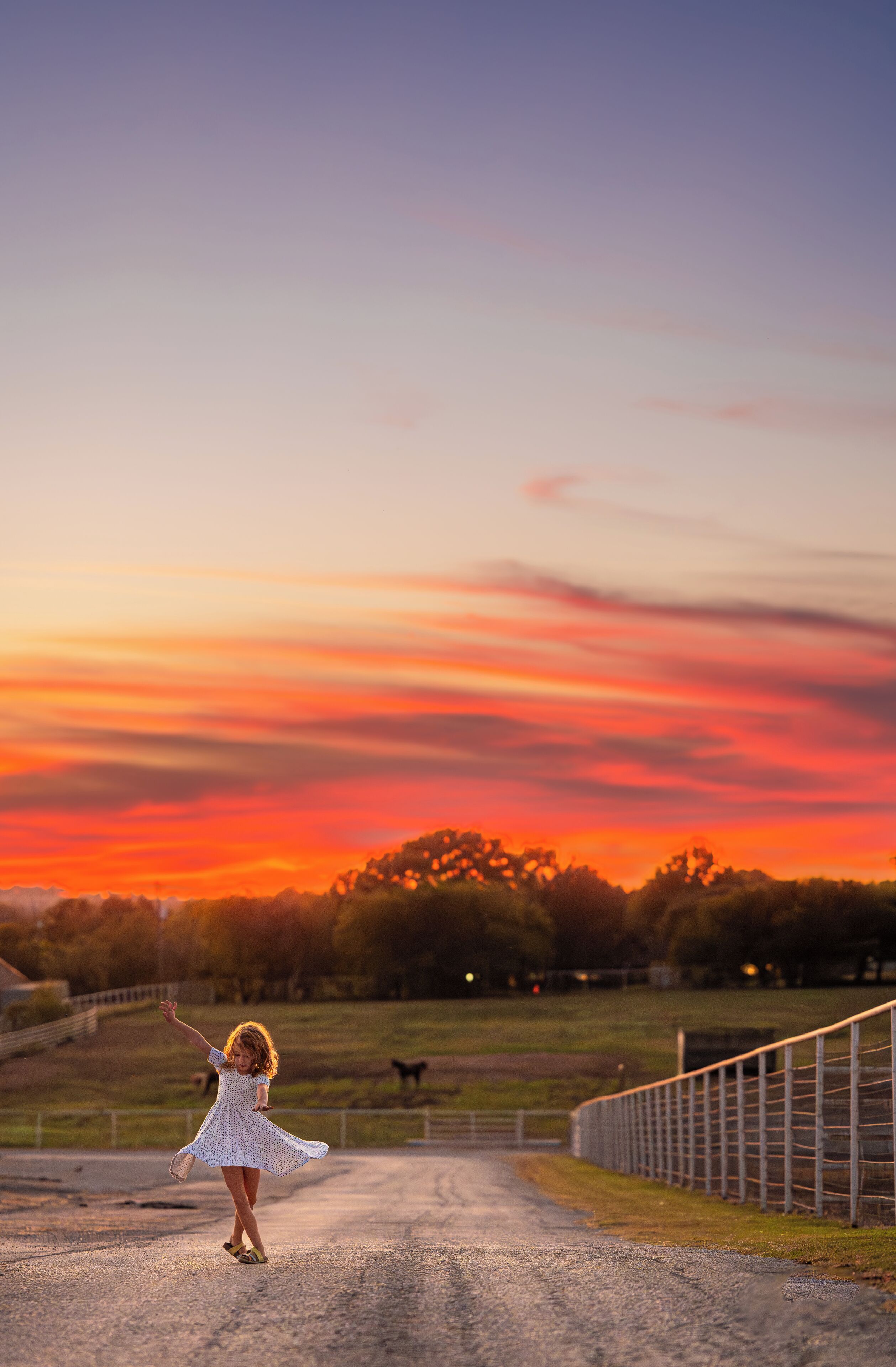 A rural road with a fence on one side and a sunset in the background.