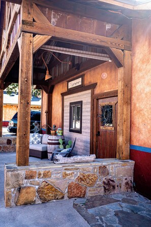A wooden porch with a stone wall, a wooden door, and a bench. - 

Escape to a cozy, four bedroom two-bath retreat on a beautiful working ranch!  (Fort Worth)