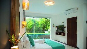 A bedroom with a bed, a TV, a window with a view of greenery, and an air conditioning unit. - Aaradhya Madu River  (Ambalangoda)