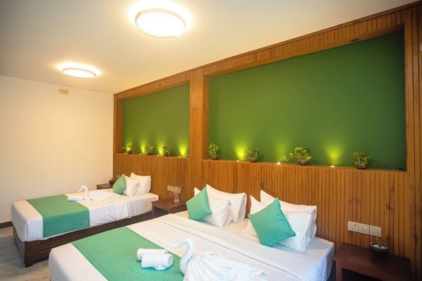 A hotel room with two beds, each with a green bedspread, white linens, and matching green pillows. There are small potted plants on the wall behind the beds.