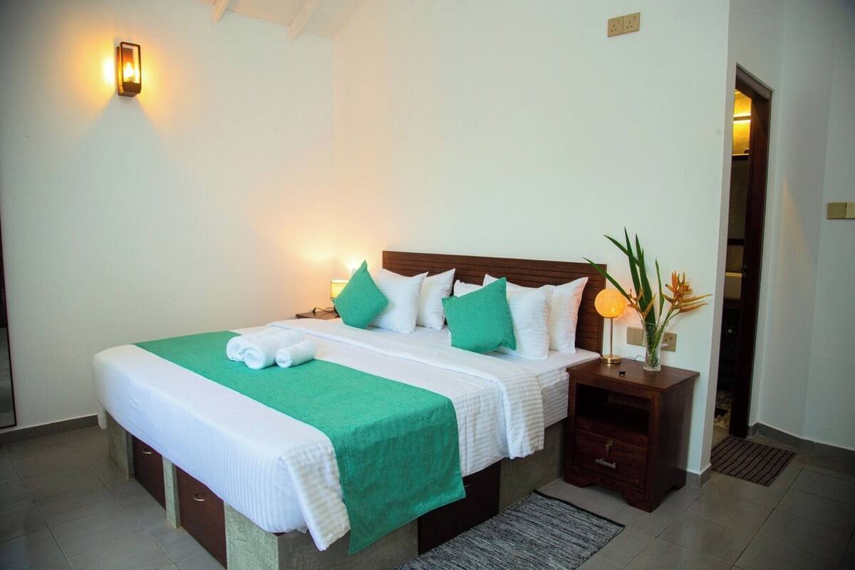 A neatly made bed with green and white bedding, a bedside lamp, and a small plant on a nightstand.