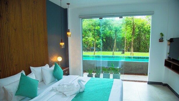 A bedroom with a large bed, a view of a swimming pool, and a balcony with potted plants. - Aaradhya Madu River  (Ambalangoda)