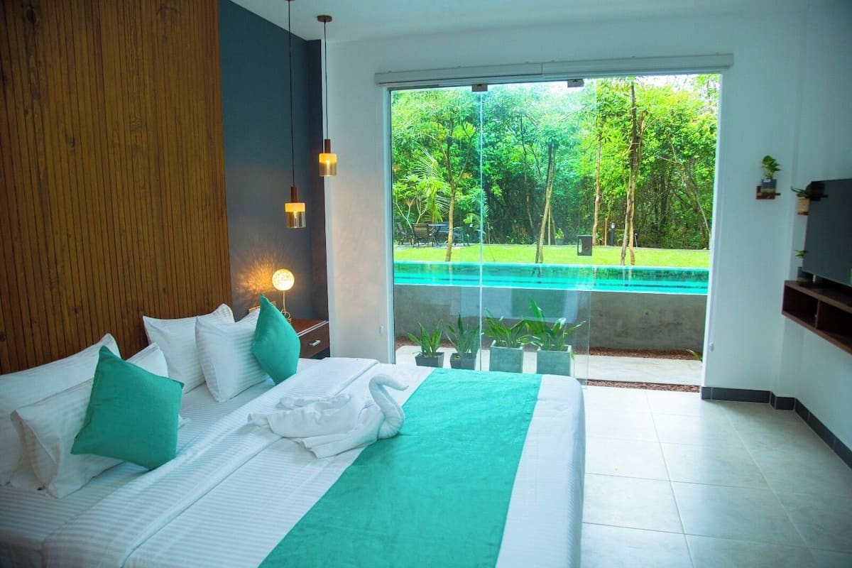 A bedroom with a large bed, a view of a swimming pool, and a balcony with potted plants.