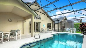 An indoor swimming pool with a glass ceiling, lounge chairs, and a dining area with striped chairs. - Golfview 4 bedroom villa with pool in Southern Dunes, 20 miles from Disneyworld (Haines City)