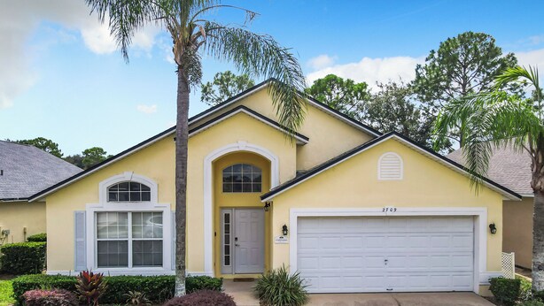 A yellow two-story house with a white garage door, a front entrance, and a small front yard with landscaping. - Golfview 4 bedroom villa with pool in Southern Dunes, 20 miles from Disneyworld (Haines City)