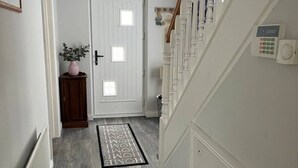 Een hal met een witte deur, een klein plantje, een grijze vloerkleed en een thermostaat aan de muur.