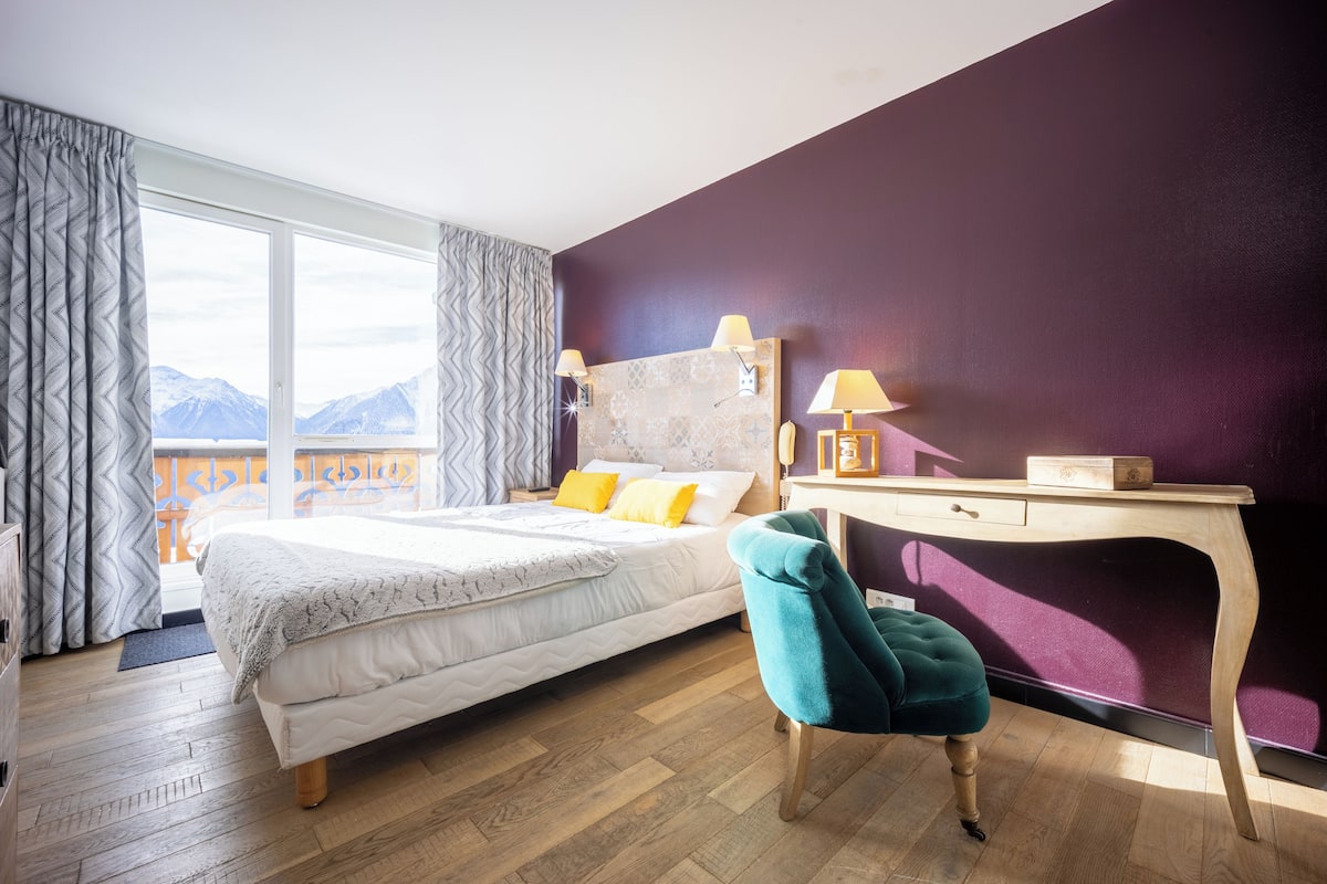 A bedroom with a bed, a desk, a chair, and a view of mountains.