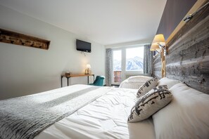 Habitación de hotel con cama, escritorio, silla, televisor y vista a las montañas.