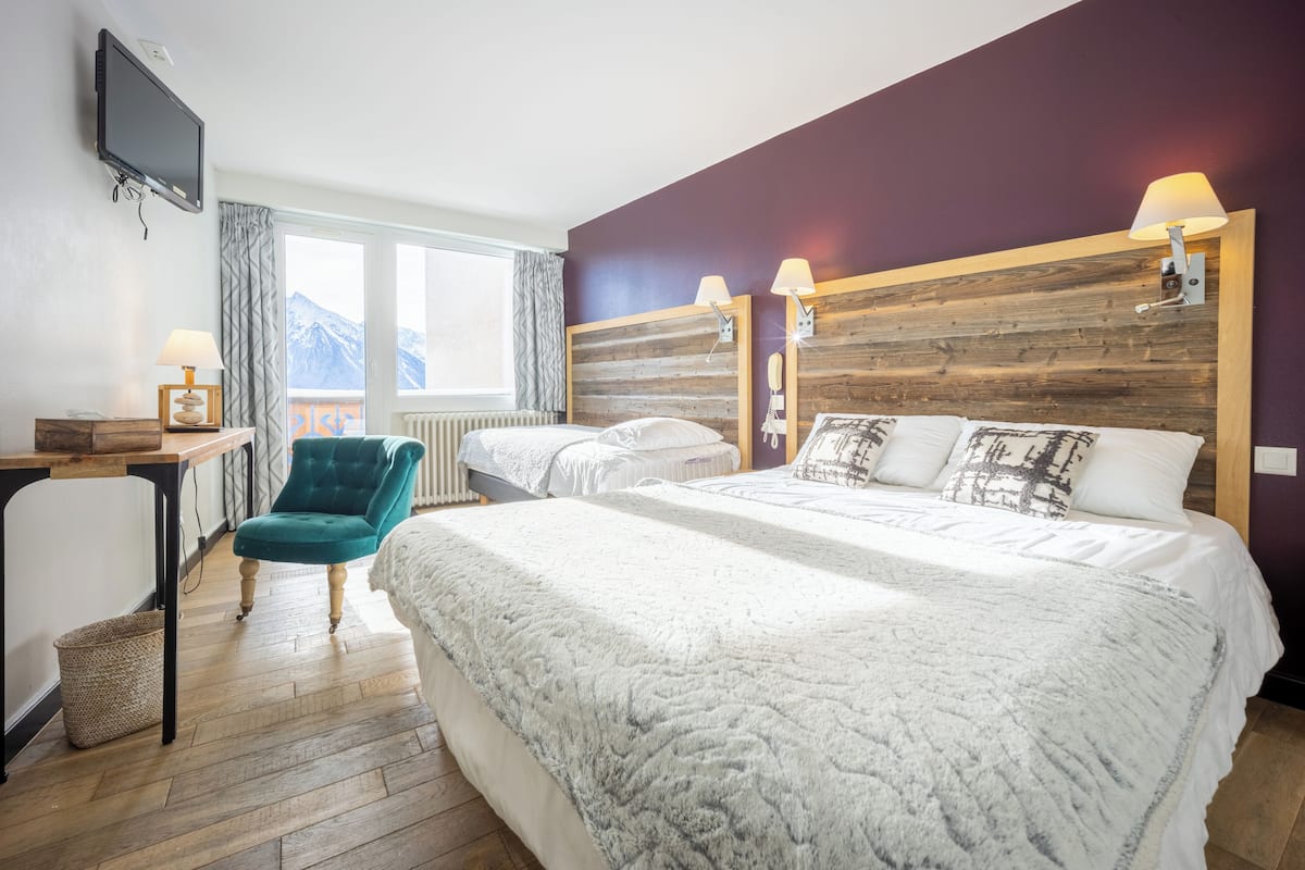 A hotel room with a large bed, a desk, a chair, and a view of mountains through the window.