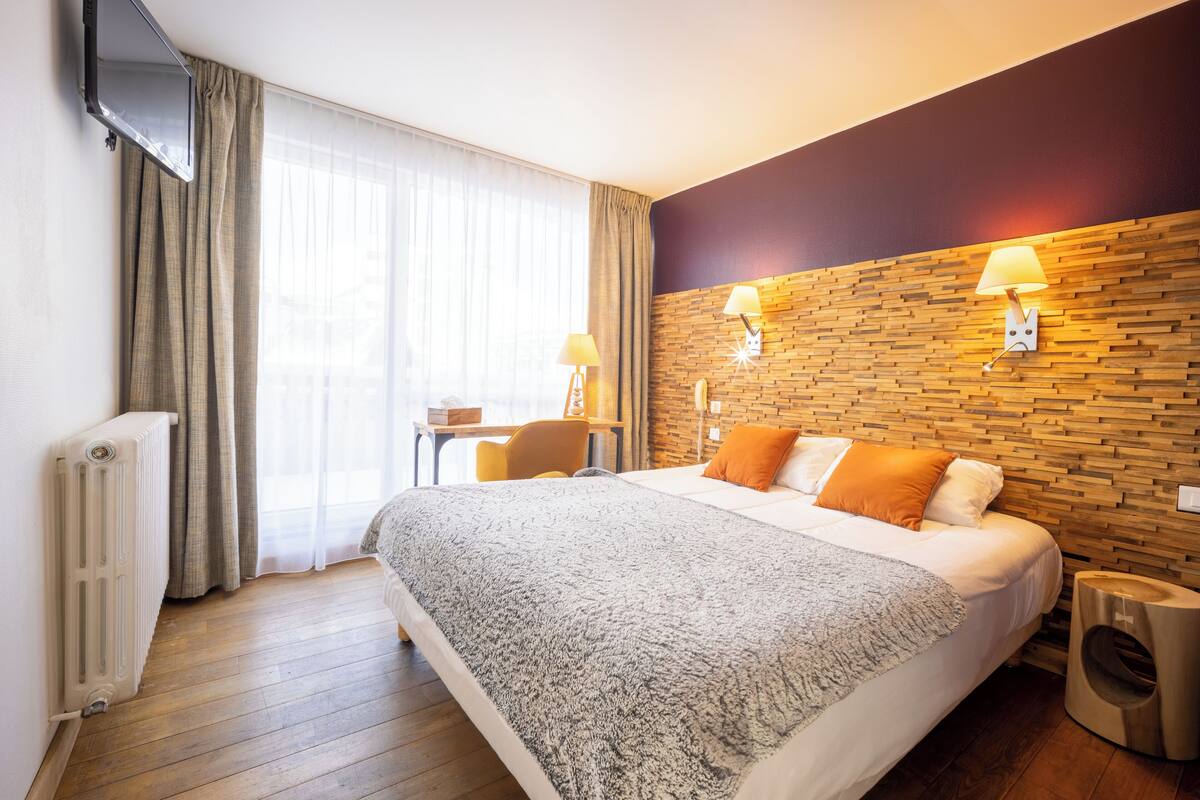 A hotel room with a large bed, a wooden accent wall, a desk, and a chair.
