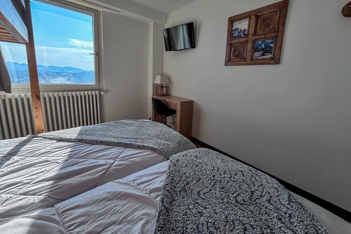 A bedroom with a large bed, a TV mounted on the wall, and a window overlooking a mountainous landscape.