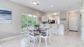 A spacious kitchen with white cabinets, a dining area with a table and chairs, and a large window providing a view of greenery outside. - Gulf Walk 506 (Miramar Beach)