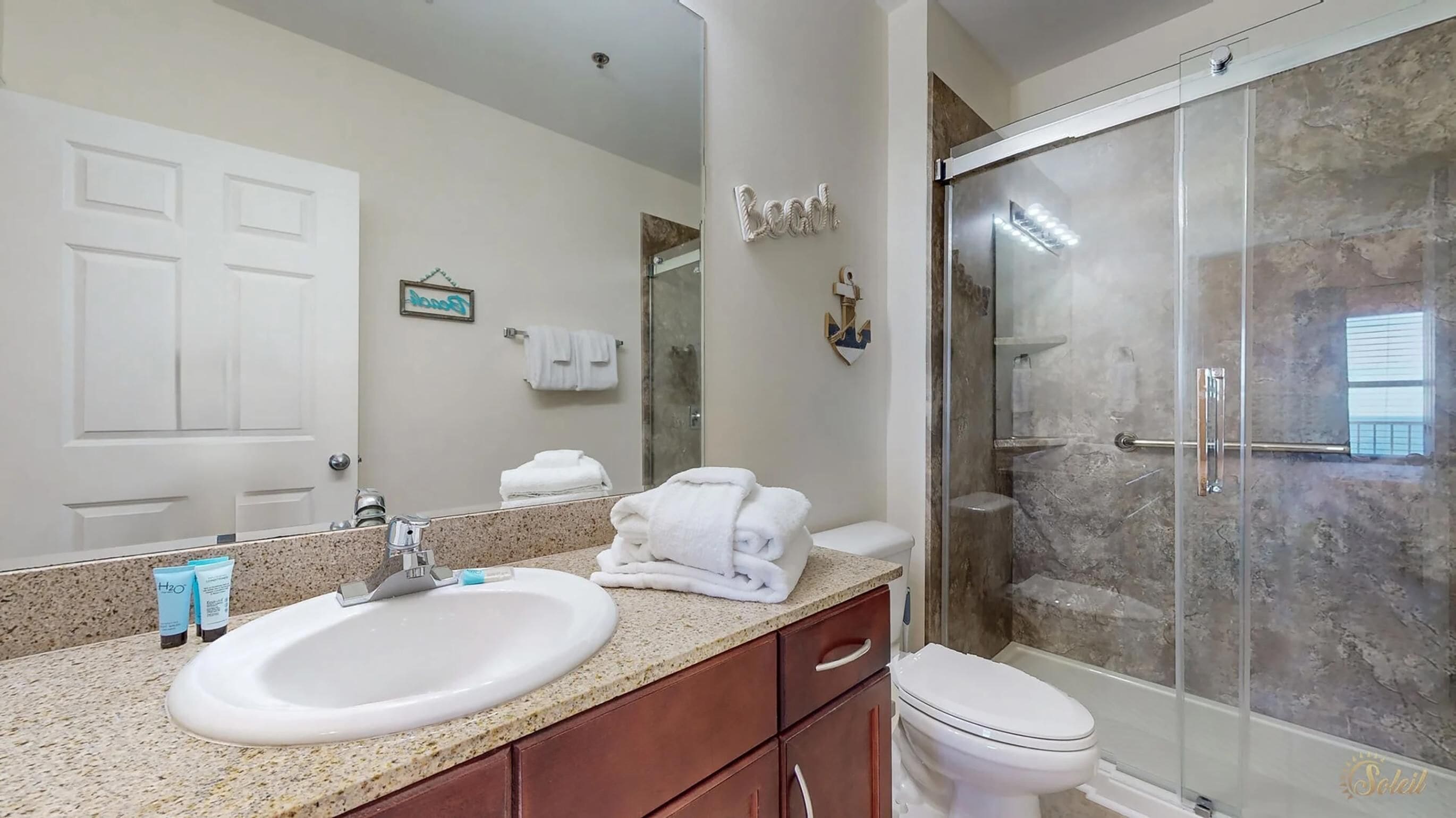 A bathroom with a white sink, a mirror, a glass shower enclosure, and a toilet.