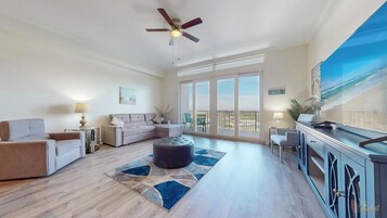 A spacious living room with a ceiling fan, a sofa, a coffee table, and a view of the balcony.