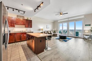 Eine moderne Küche mit Holzschränken, einem Edelstahlkühlschrank und einer großen Kochinsel. Es gibt einen Essbereich mit Tisch und Stühlen sowie einen Balkon mit Blick.