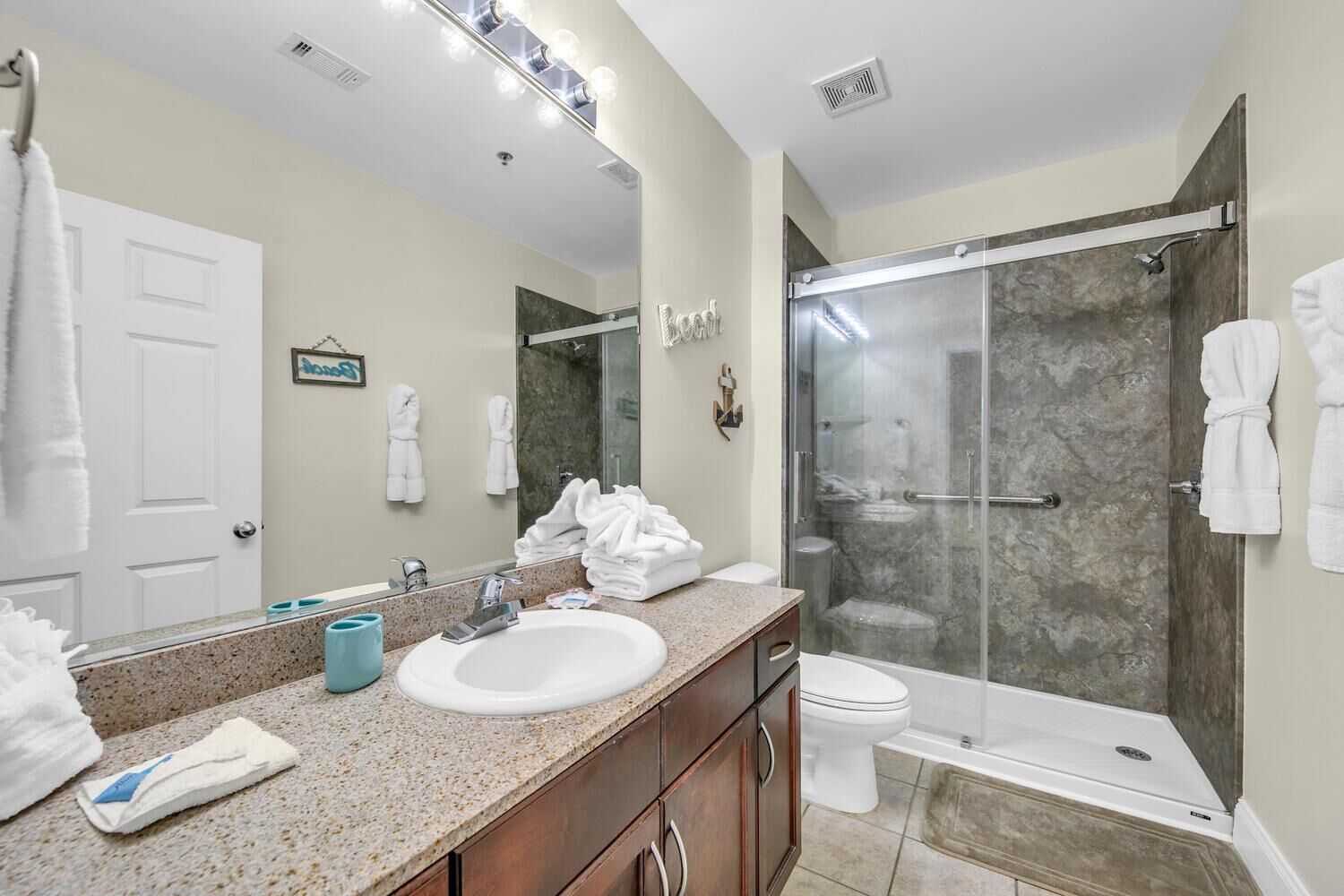 A modern bathroom with a granite countertop, white sink, and a glass-enclosed shower.
