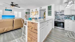 Een moderne keuken met witte kastjes, een centraal eiland en een zithoek met een beige bank.