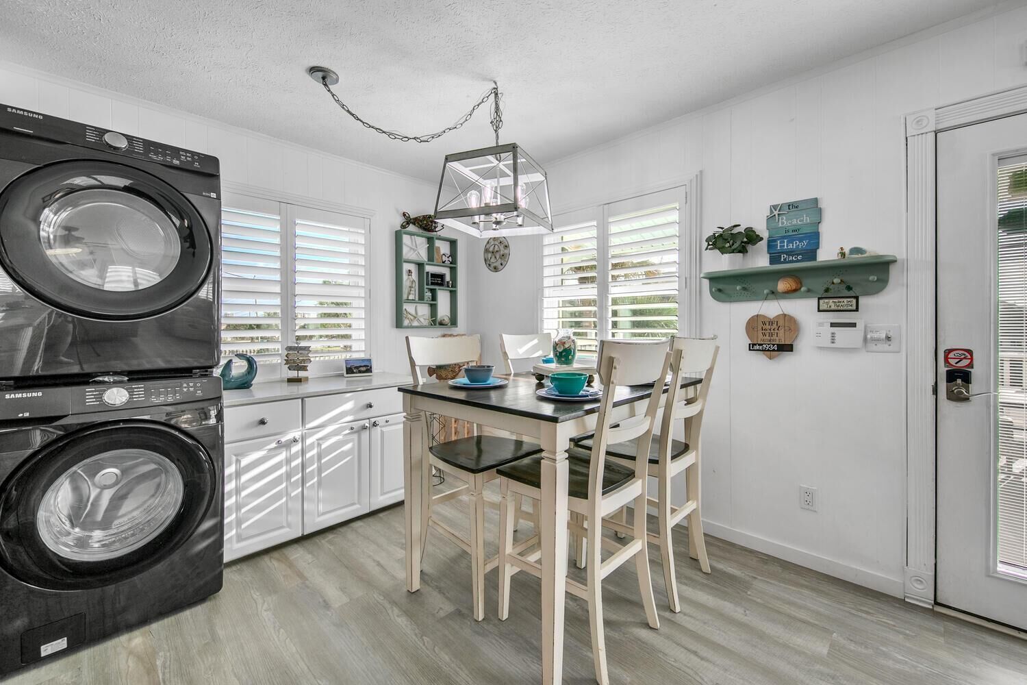 A compact kitchen with a washing machine, a dining table with chairs, and a hanging light fixture.