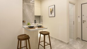 Uma cozinha moderna com revestimento de mármore, bancada branca, dois banquinhos de madeira e uma moldura com imagem na parede.