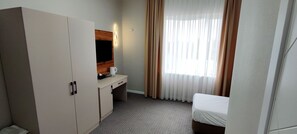 A hotel room with a wardrobe, a desk with a flat-screen TV, a bed, and a window with curtains. - Cozy Hotel (Bishkek)